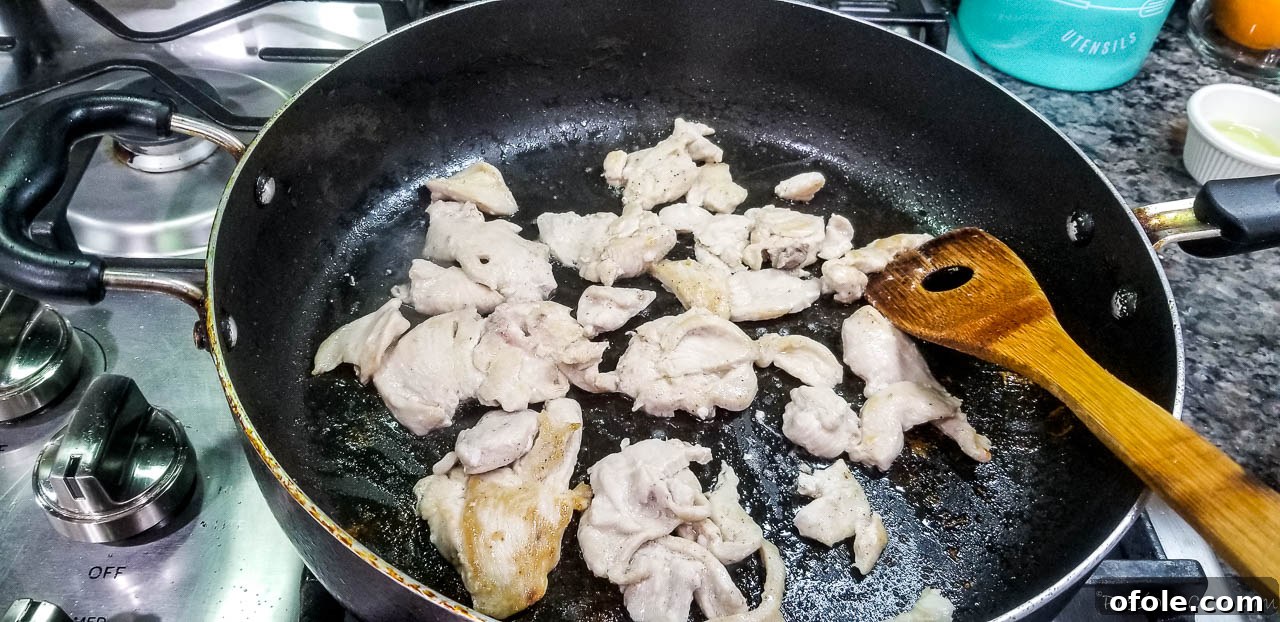 Thinly sliced chicken breasts cooking in a hot wok or large pan, turning golden brown.