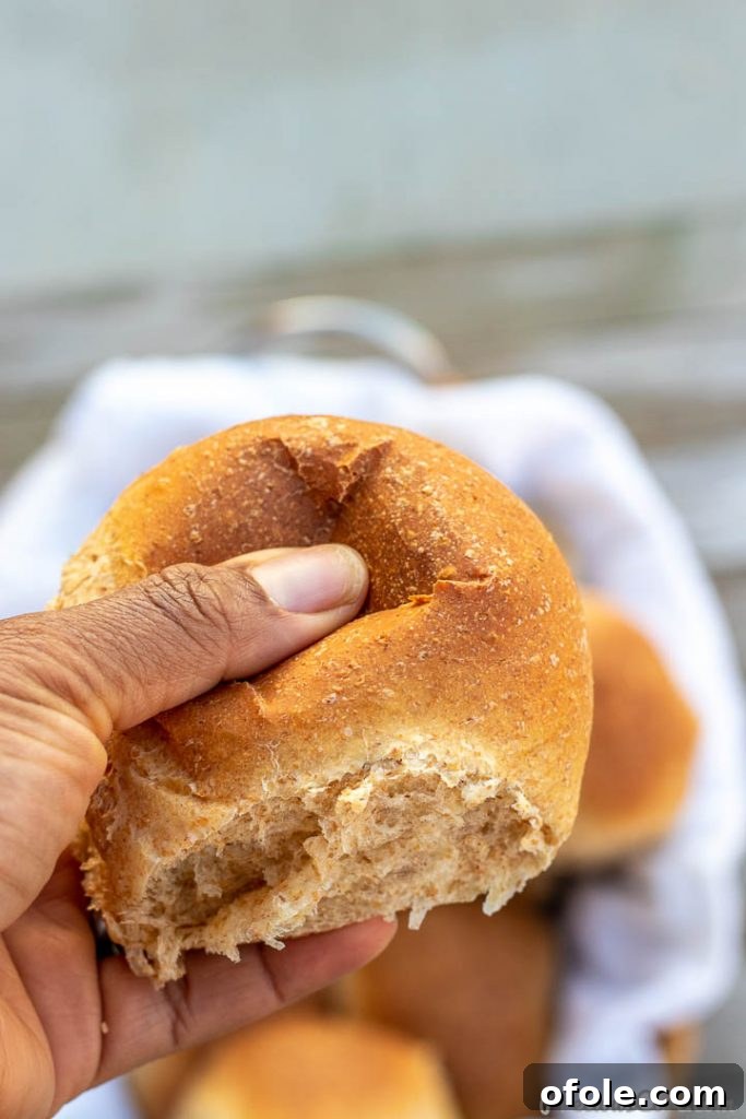 Honey Kissed Whole Wheat Dinner Rolls 4 A hand gently pressing on a freshly baked, soft dinner roll, highlighting its tender texture.