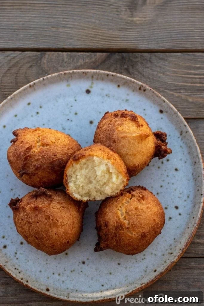 Heavenly Coconut Doughnuts 2 Golden brown coconut doughnuts arranged on a white plate, with one doughnut cut open to show its soft, cakey texture