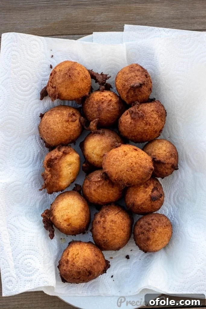Heavenly Coconut Doughnuts 5 Freshly fried coconut doughnuts resting on paper towels to drain excess oil, showcasing their perfect golden-brown color