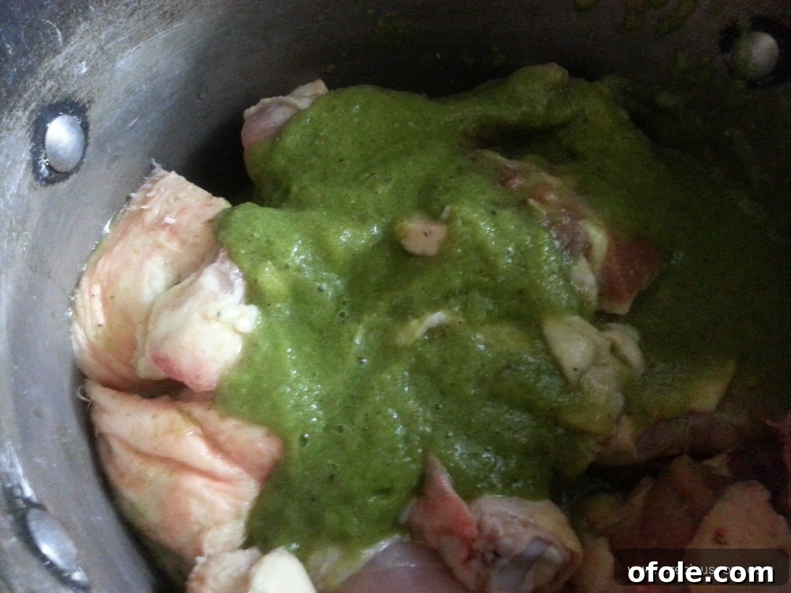 Freshly blended aromatic spices (garlic, ginger, herbs, onion) being poured over raw chicken pieces in a pot.