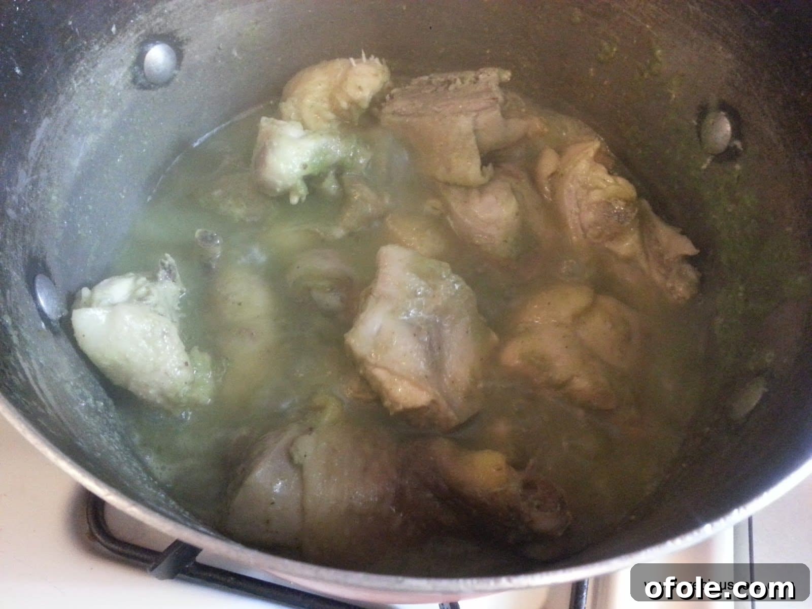Chicken simmering in a pot with broth and spices, creating a rich aroma.