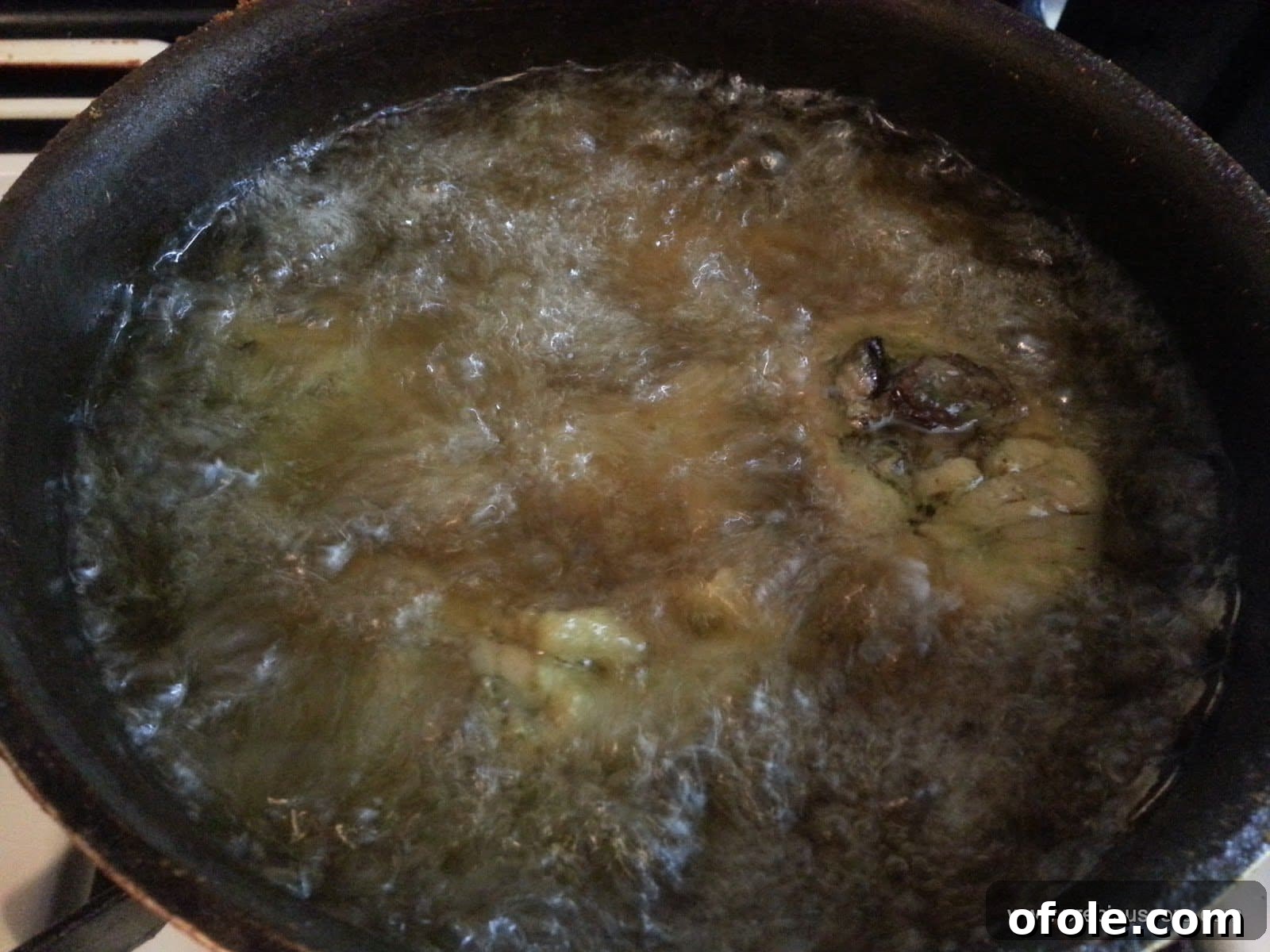 Chicken pieces sizzling and browning in hot oil during the frying process.