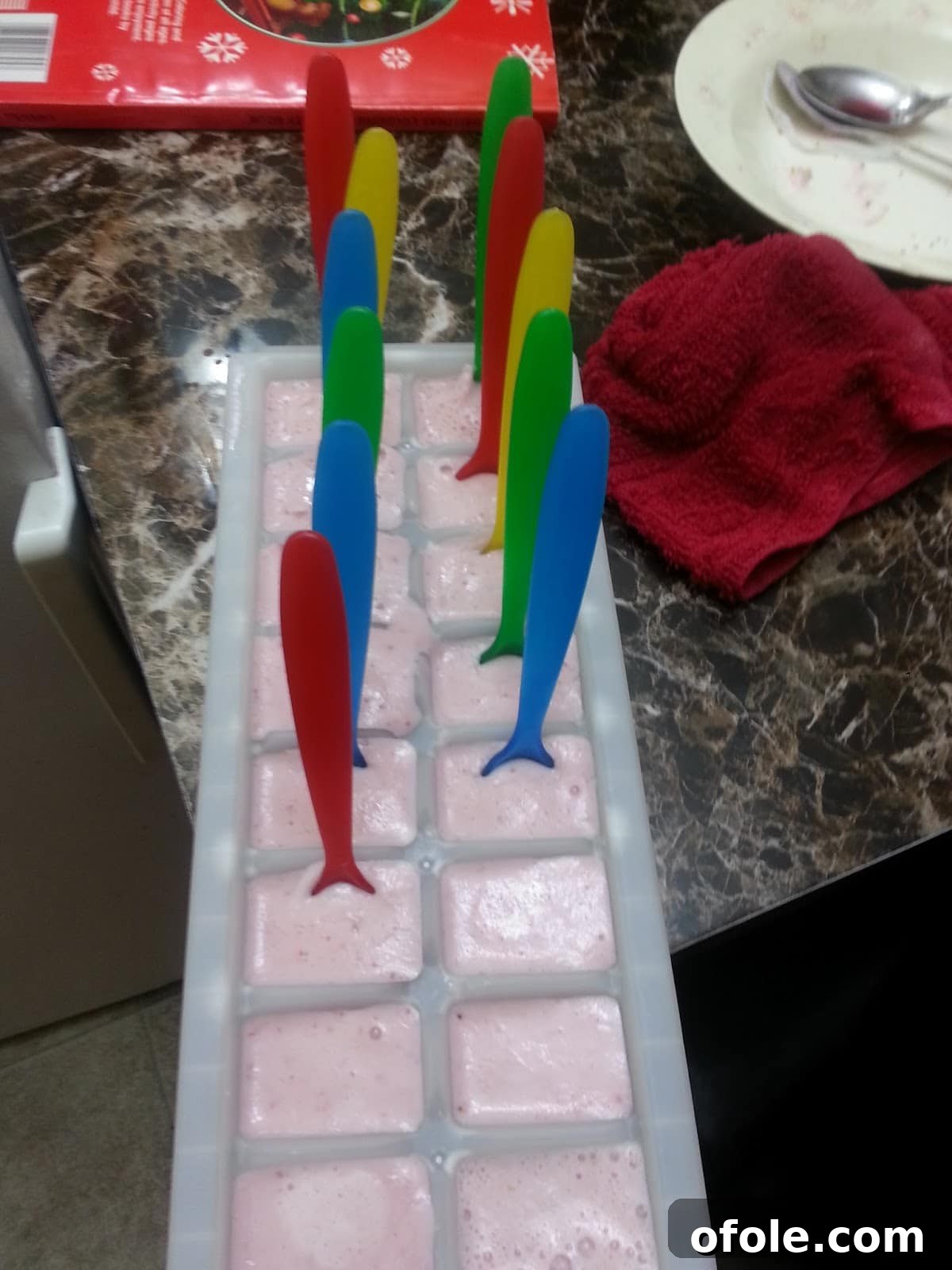 Popsicle sticks inserted into partially frozen yogurt and fruit mixture in ice cube trays