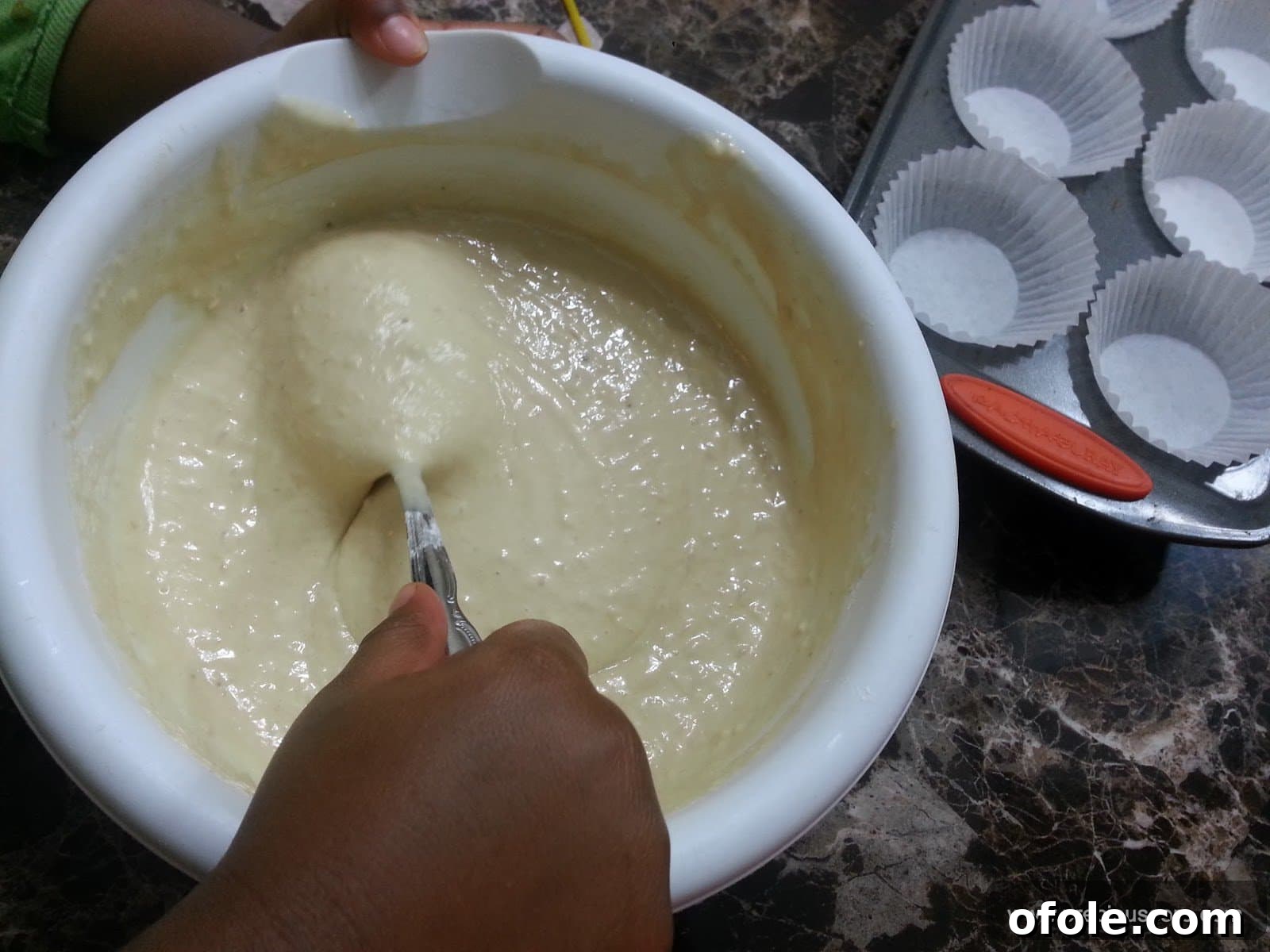 Spoon stirring a bowl of banana cake batter.