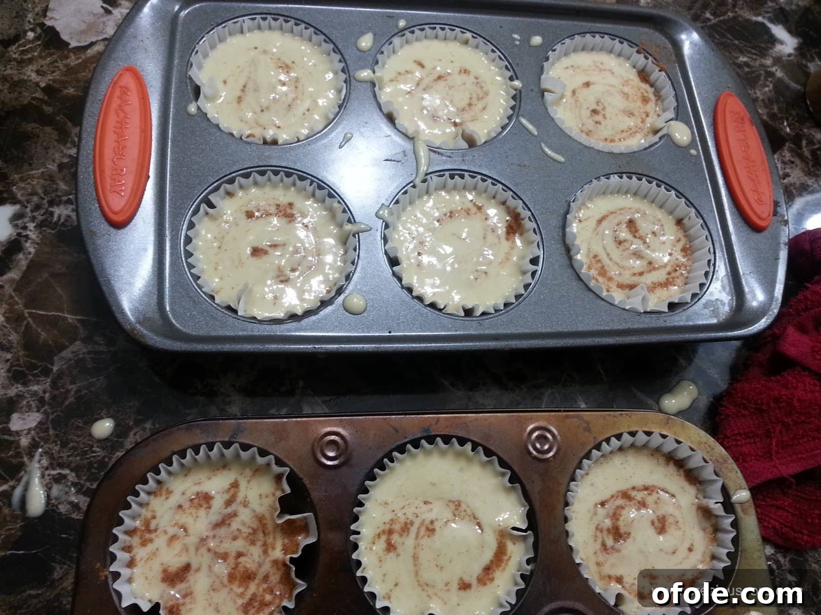 Muffin pan full of banana cake batter with cinnamon lightly swirled.