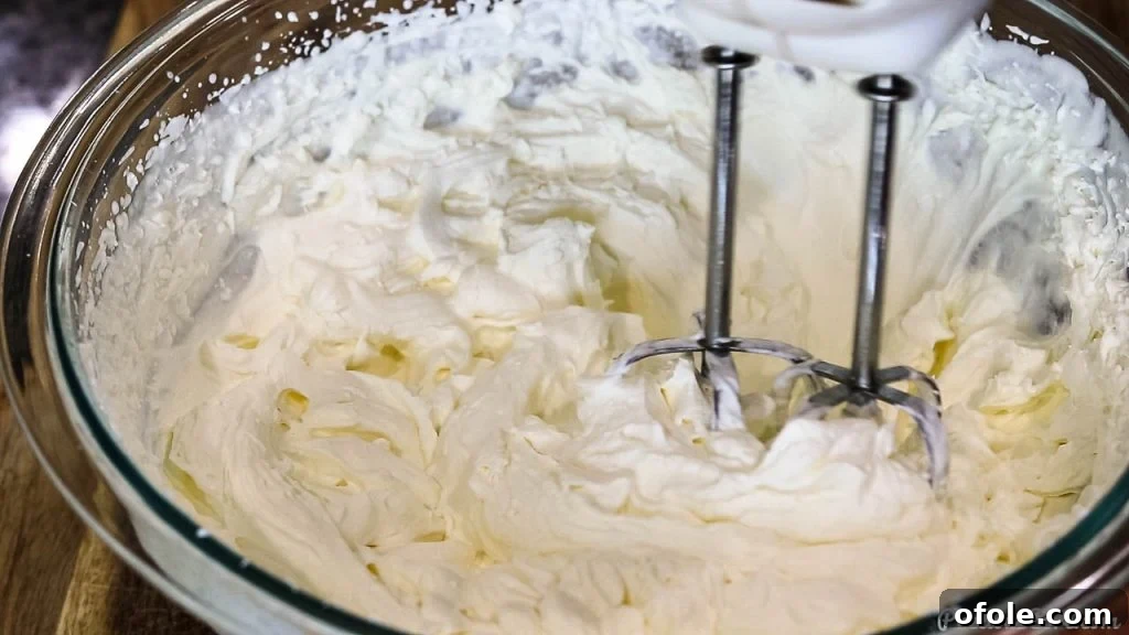 Close-up shot of heavy whipping cream being beaten to stiff peaks in a large mixing bowl, illustrating the perfect consistency.