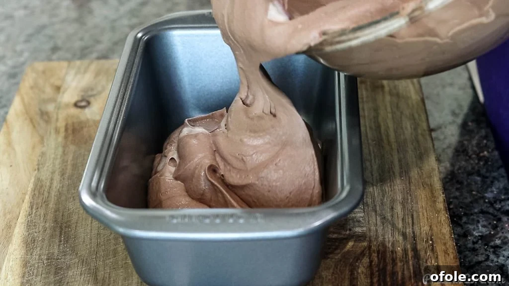 Pouring the chocolate ice cream mixture into a metal loaf pan, ensuring an even distribution for freezing.