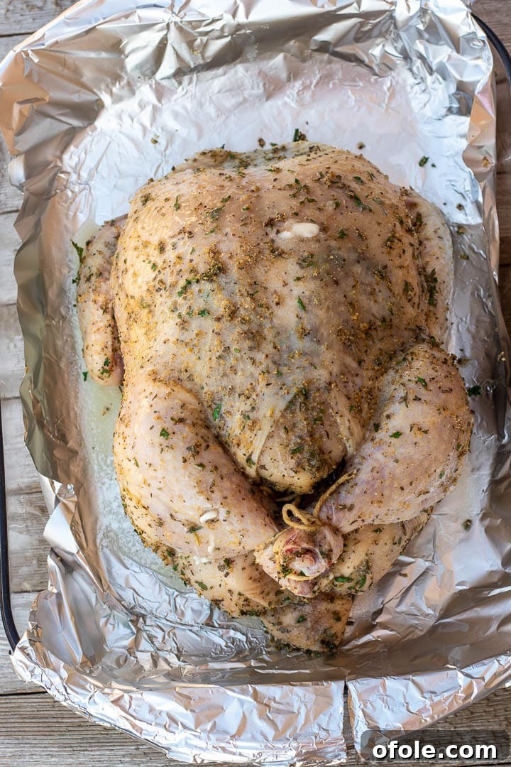 Savory Herb Roasted Chicken 6 Seasoned whole chicken in a baking dish, ready for roasting, with legs tied with kitchen twine.