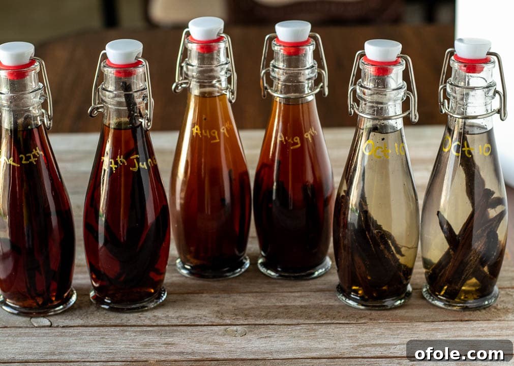 Three glass bottles of homemade vanilla extract, varying in color from light amber to deep brown, displayed on a wooden surface.