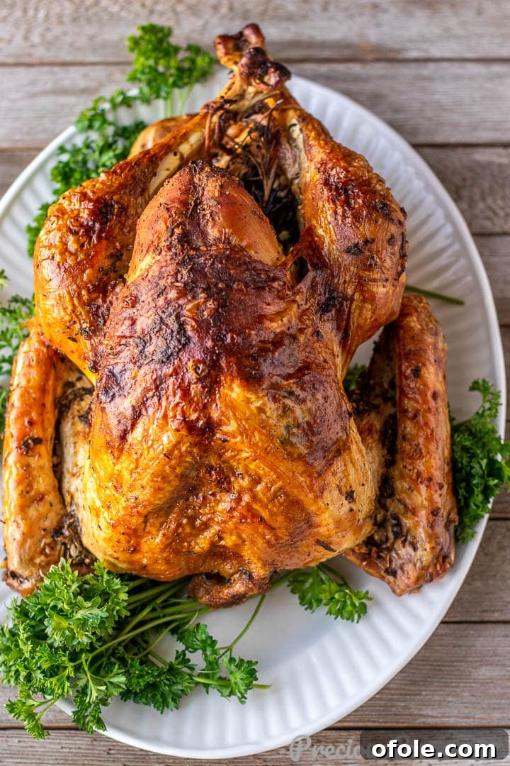 A whole herb roasted turkey resting on a large serving platter, lightly tented with aluminum foil to allow juices to redistribute.