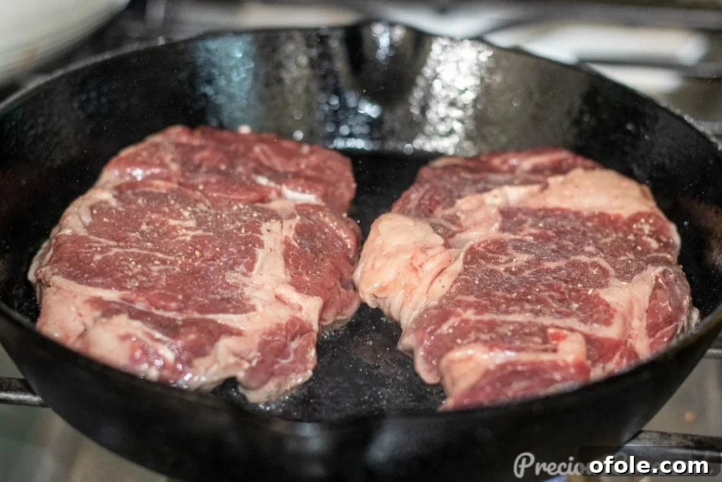 Searing Ribeye in Cast Iron A raw ribeye steak sizzling in a hot cast iron skillet, beginning to develop a sear.