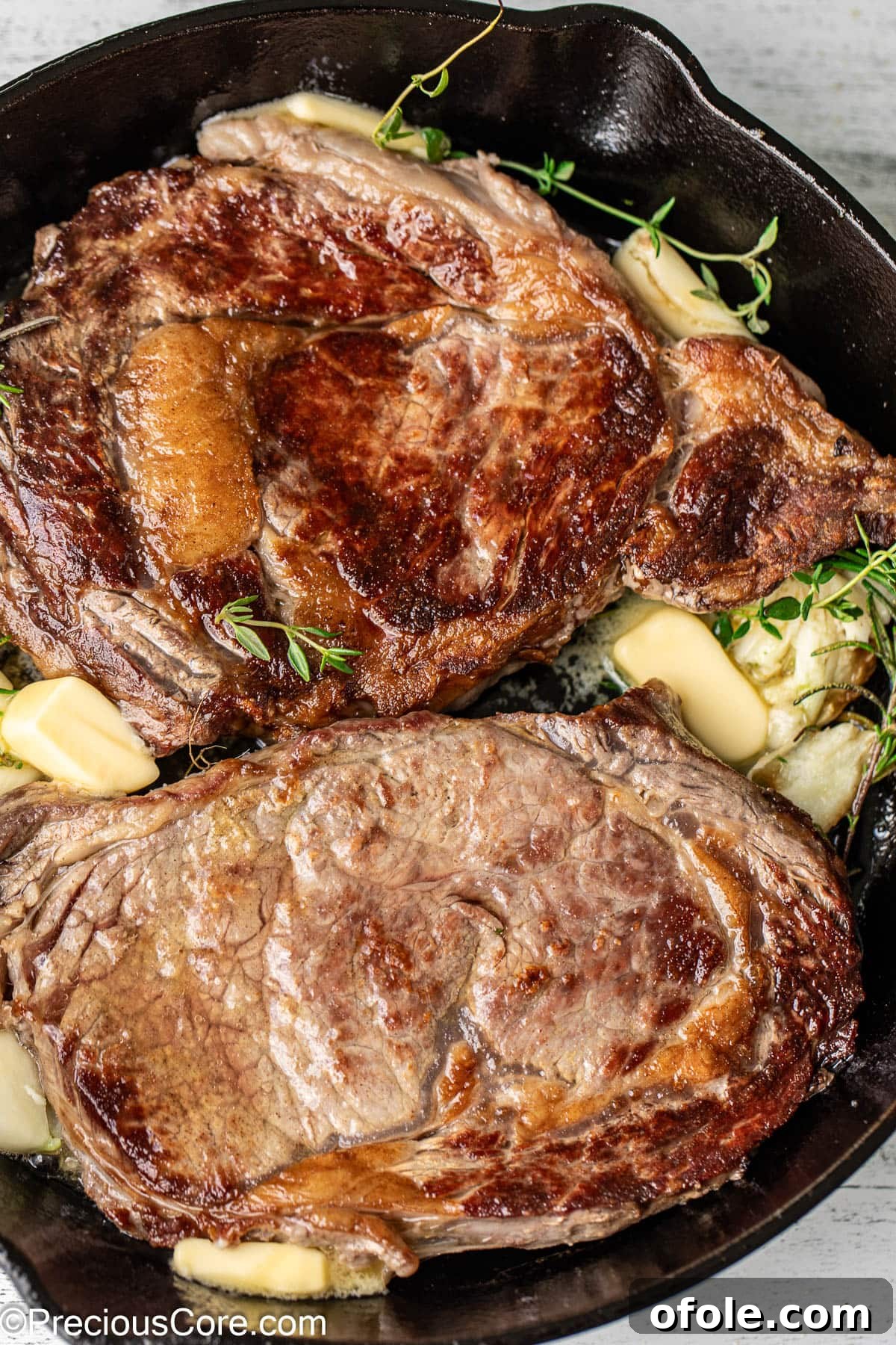 Basting Ribeye with Herb Butter Two ribeye steaks actively sizzling in a cast iron skillet with melted butter, garlic, rosemary, and thyme, being basted.
