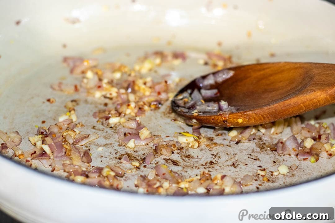 Diced onions and minced garlic gently sautéing in a hot pan with olive oil, creating a fragrant aromatic base.