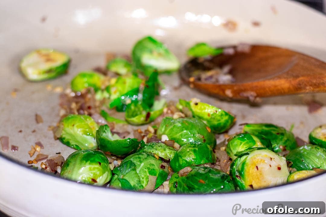 Brussels sprouts added to the hot pan, beginning to sauté with the aromatics, ensuring they cook thoroughly.
