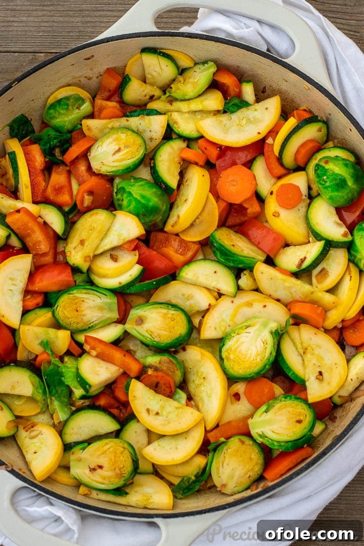 A large serving of colorful sautéed vegetables in a deep cooking pot or braiser, steaming gently and ready to be enjoyed.