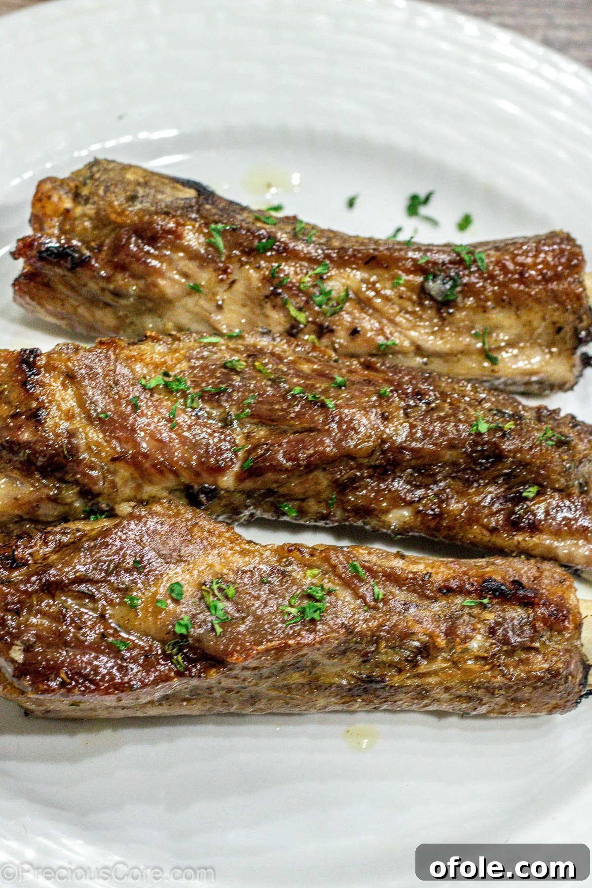 Three perfectly baked dry rub ribs resting on a pristine white plate, showcasing their rich, caramelized crust and inviting texture.