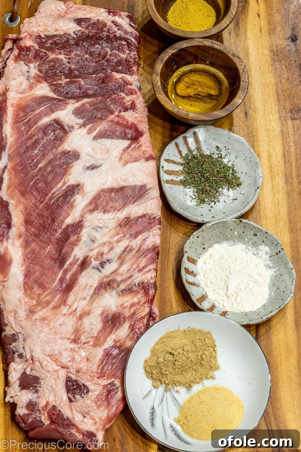 Raw spare ribs, an array of colorful spices, and coarse salt are neatly arranged on a wooden chopping board, ready for the perfect dry rub.