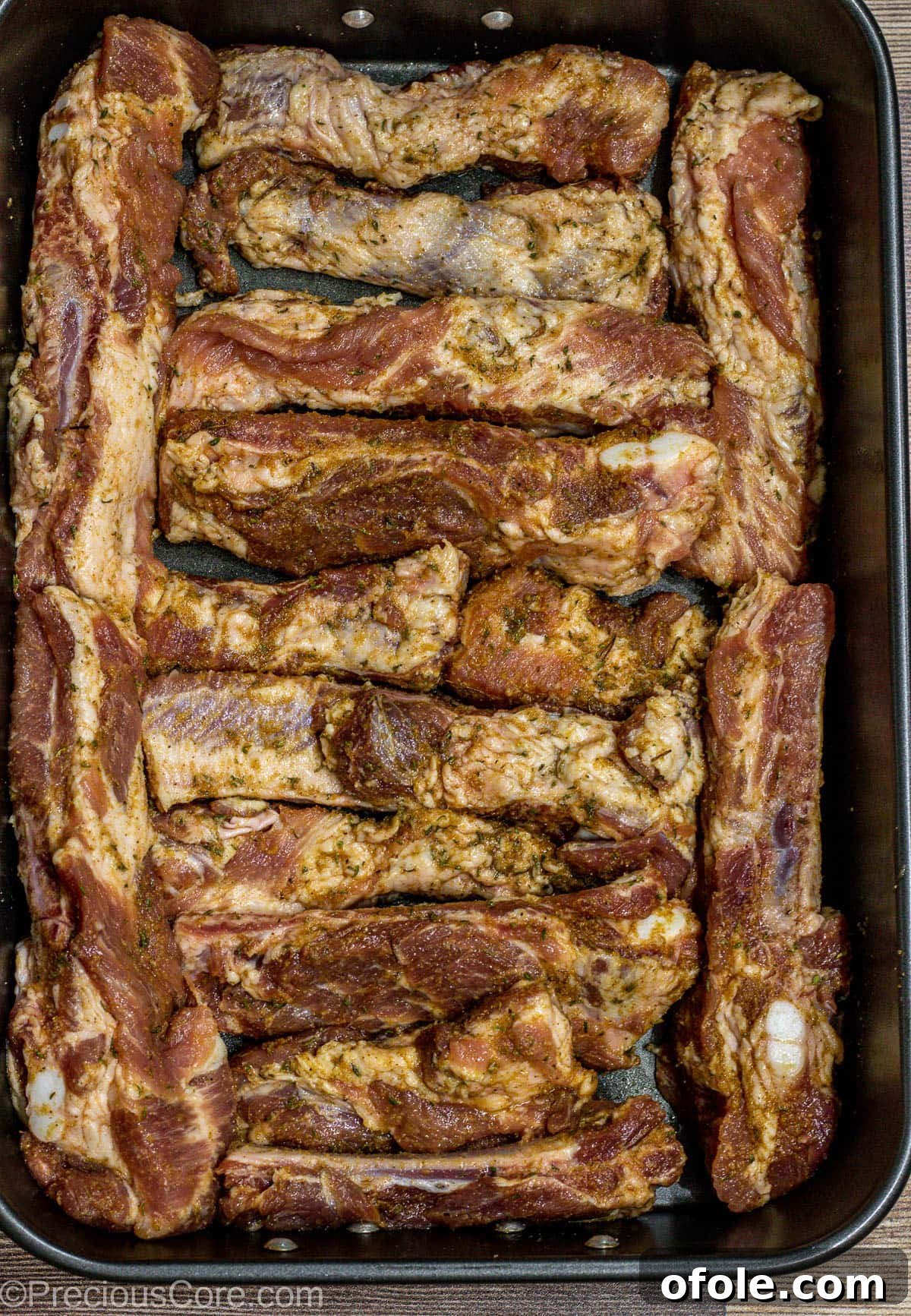 Individual seasoned ribs, glistening with dry rub, are neatly arranged in a baking dish, ready for their slow cook in the oven.