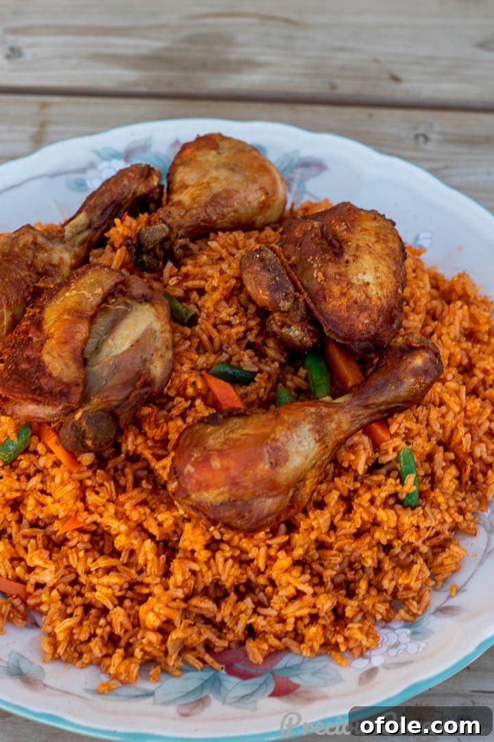 A closer, landscape shot of rich, red Jollof Rice on a serving platter, with crispy chicken pieces nestled amongst it