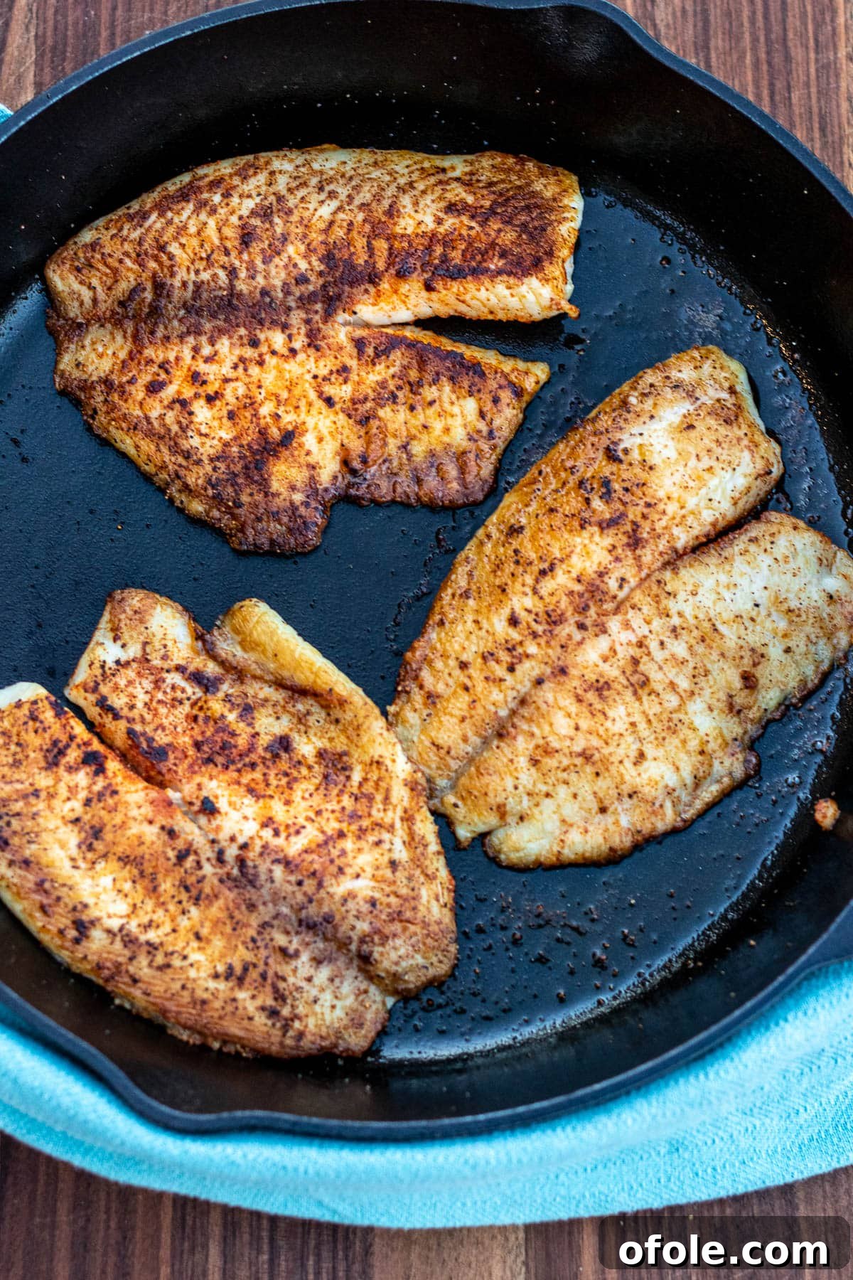 Tilapia fillets cooking in a cast iron pan, showcasing a beautiful golden sear.
