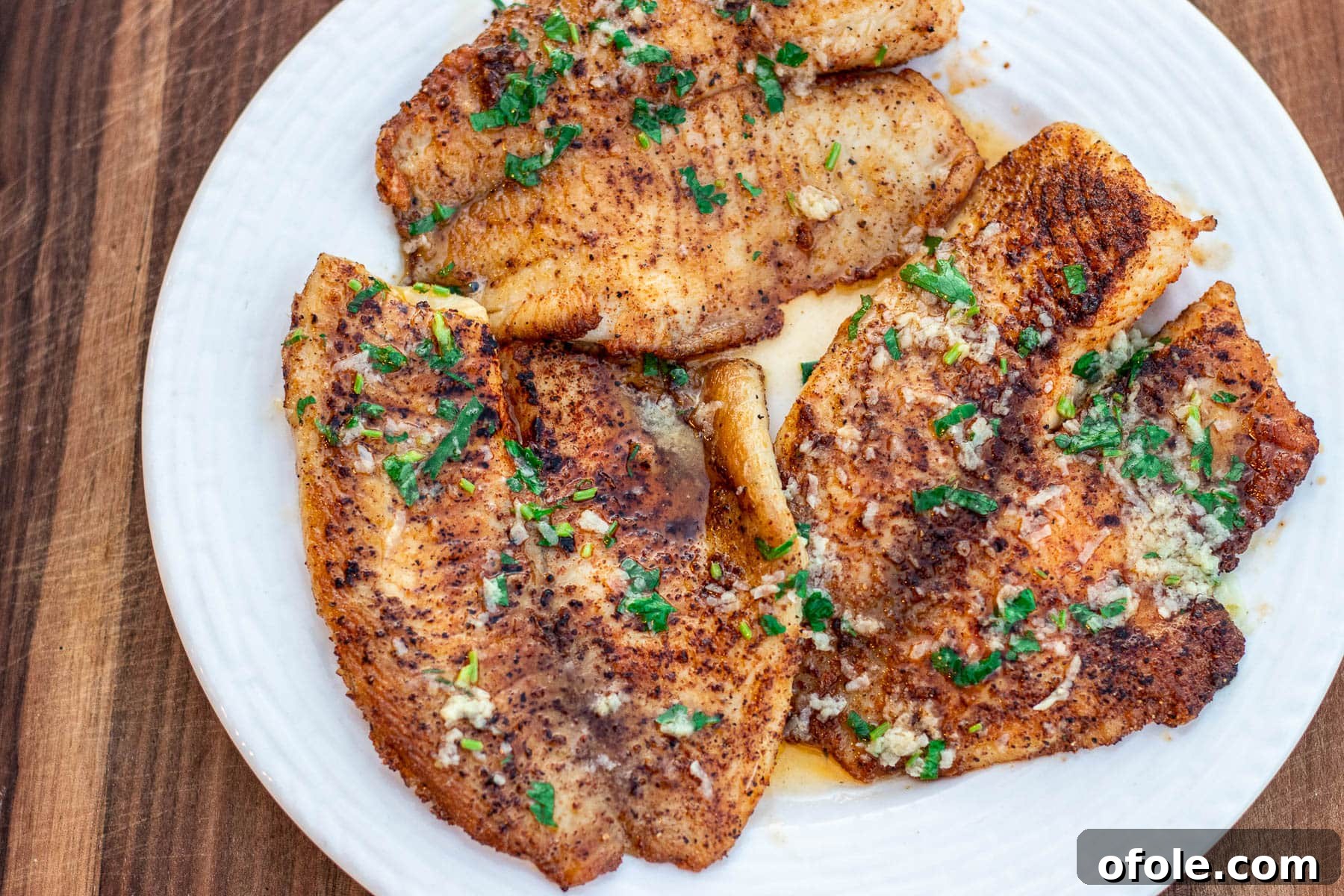 Landscape photo of freshly cooked lemon butter tilapia garnished with fresh herbs and lemon slices.