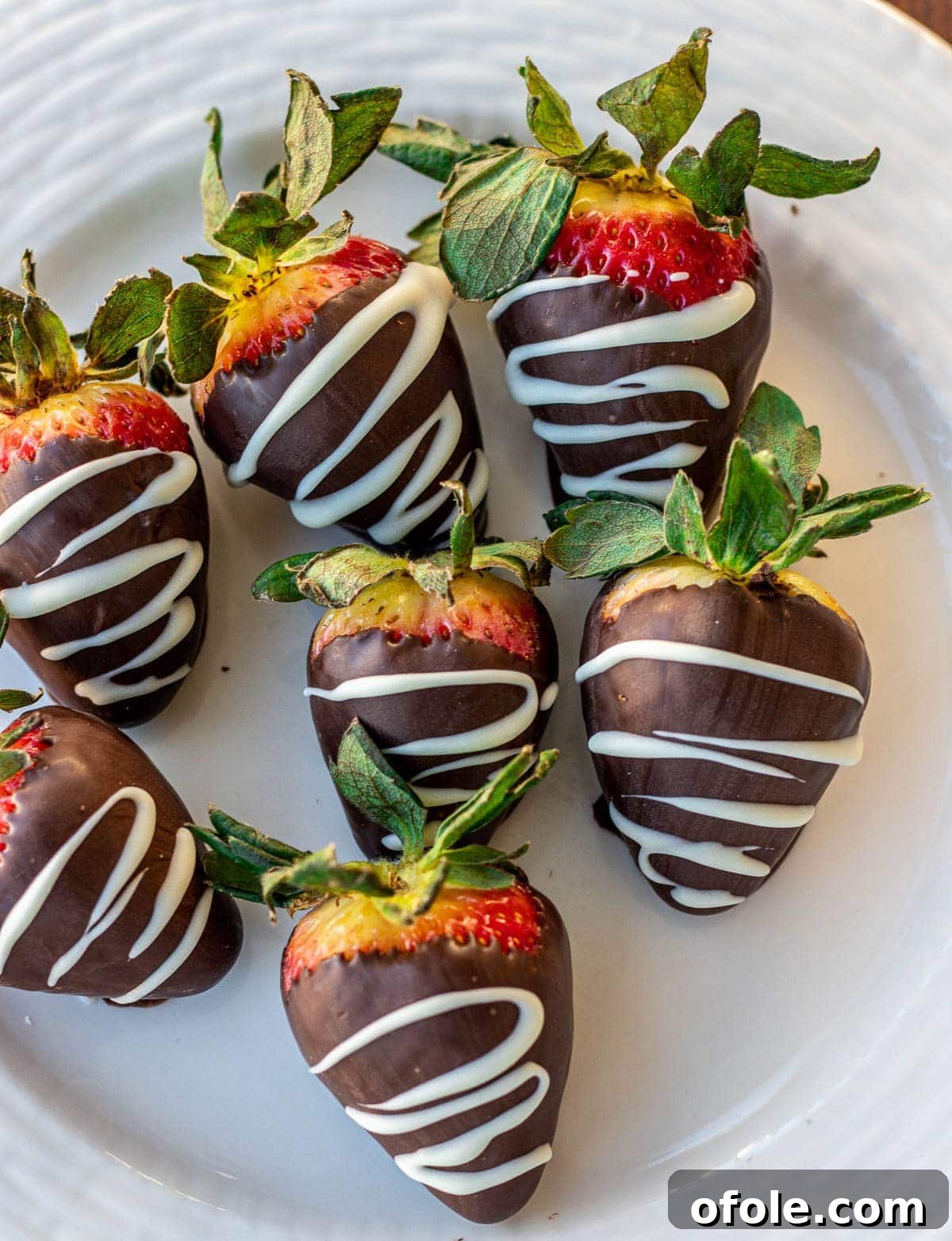 Effortless Chocolate Strawberry Indulgence 2 Freshly made chocolate dipped strawberries neatly arranged on a pristine white plate, showcasing their glossy chocolate coating.