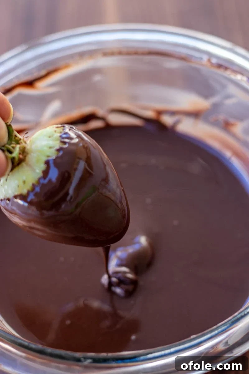 Effortless Chocolate Strawberry Indulgence 4 A hand gently dips a fresh, plump strawberry into a bowl of smooth, melted dark chocolate, capturing the moment of delicious transformation.
