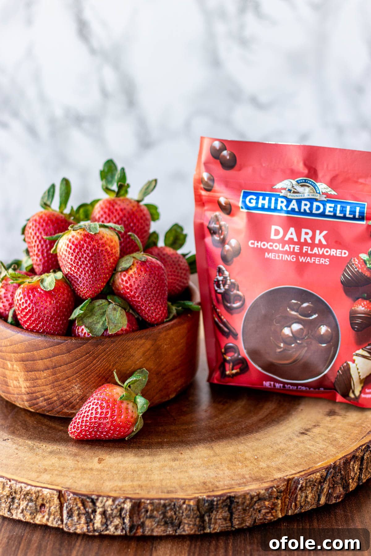 Effortless Chocolate Strawberry Indulgence 5 A bowl of vibrant red strawberries sits beside a clear bag of premium melting chocolate, ready for dipping.