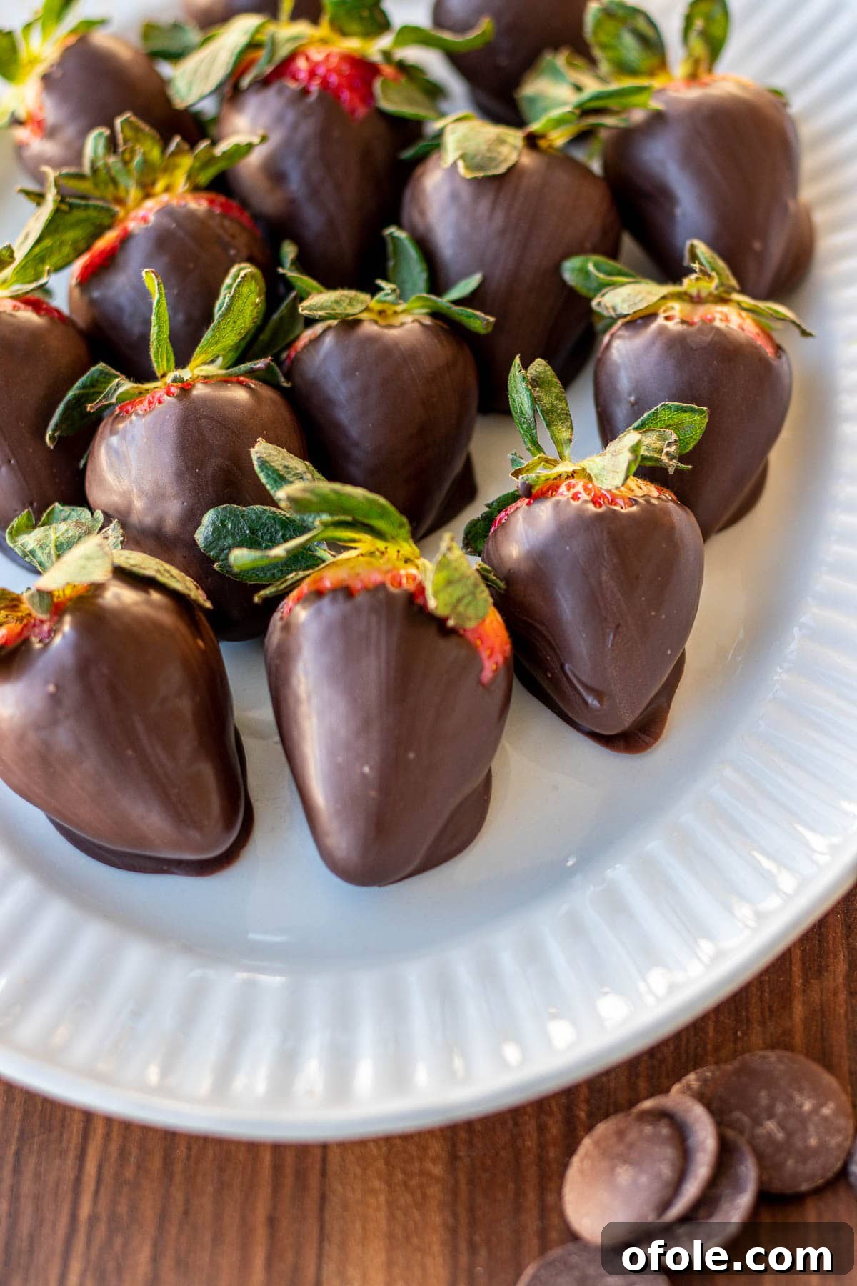 Effortless Chocolate Strawberry Indulgence 6 Several glistening strawberries coated in dark chocolate are arranged artfully on a white plate, ready to be enjoyed.