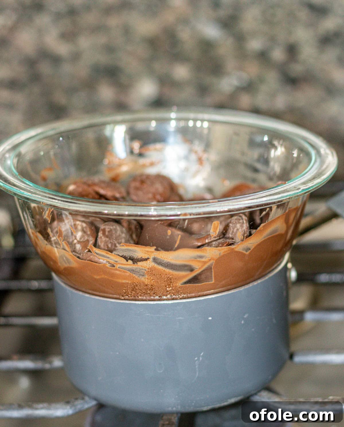 Effortless Chocolate Strawberry Indulgence 7 A glass mixing bowl filled with chocolate melting wafers rests atop a small pot of simmering water, demonstrating the double boiler method.