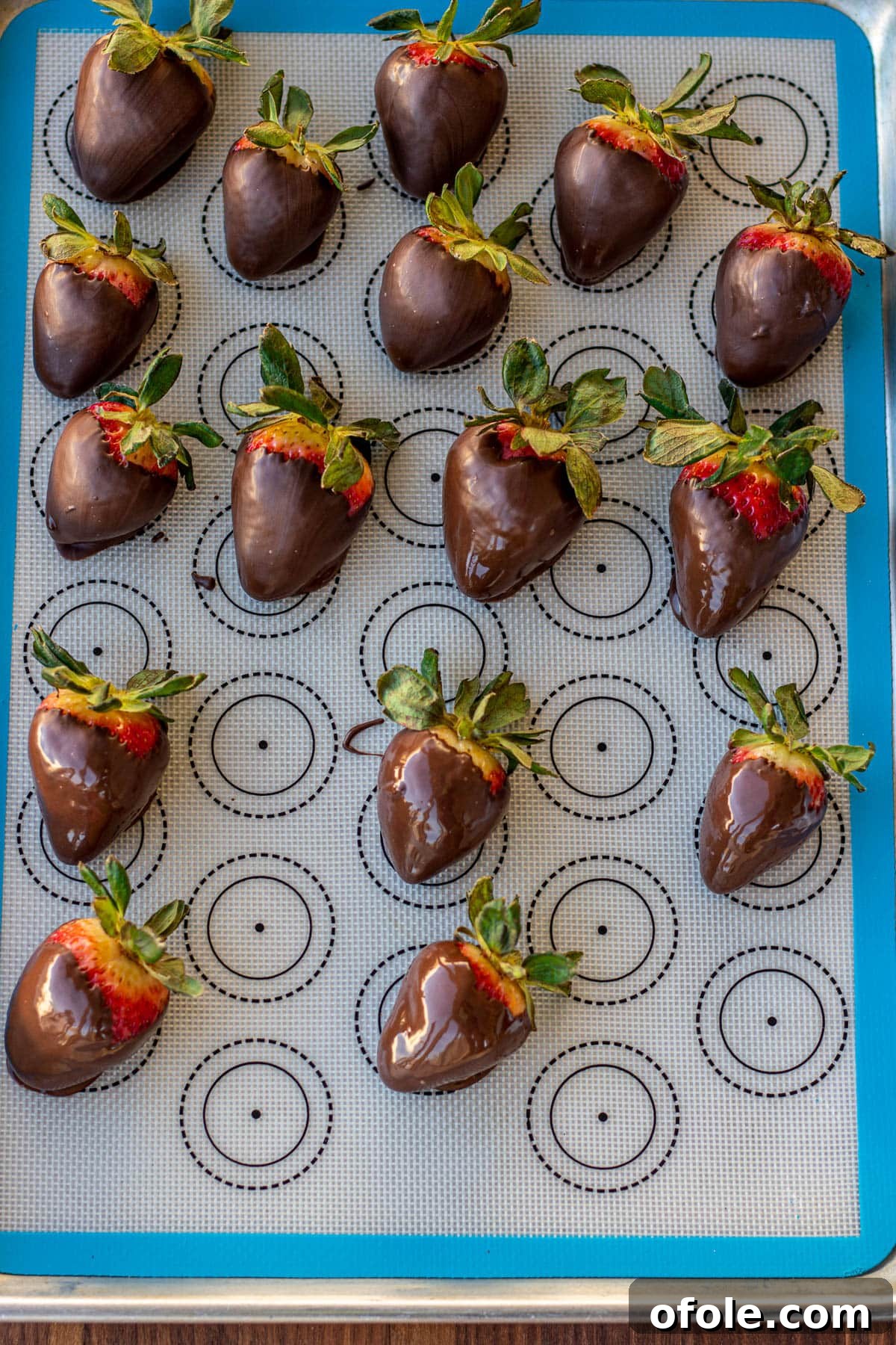 Effortless Chocolate Strawberry Indulgence 10 A tray filled with freshly coated chocolate covered strawberries rests on a silicone mat, awaiting the chocolate to set.