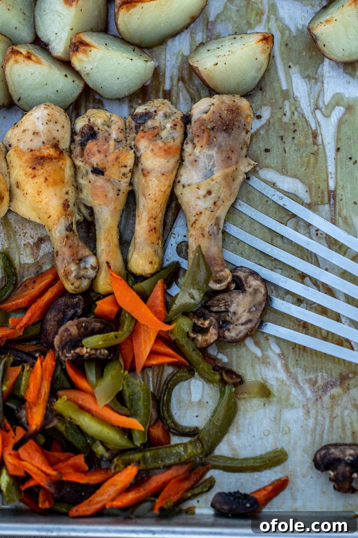 One-Pan Roasted Chicken, Potatoes, and Vegetables 7 A hand using a fish spatula to dish out a serving of the hot, freshly baked one-pan chicken, potatoes, and veggies from the sheet pan onto a plate.