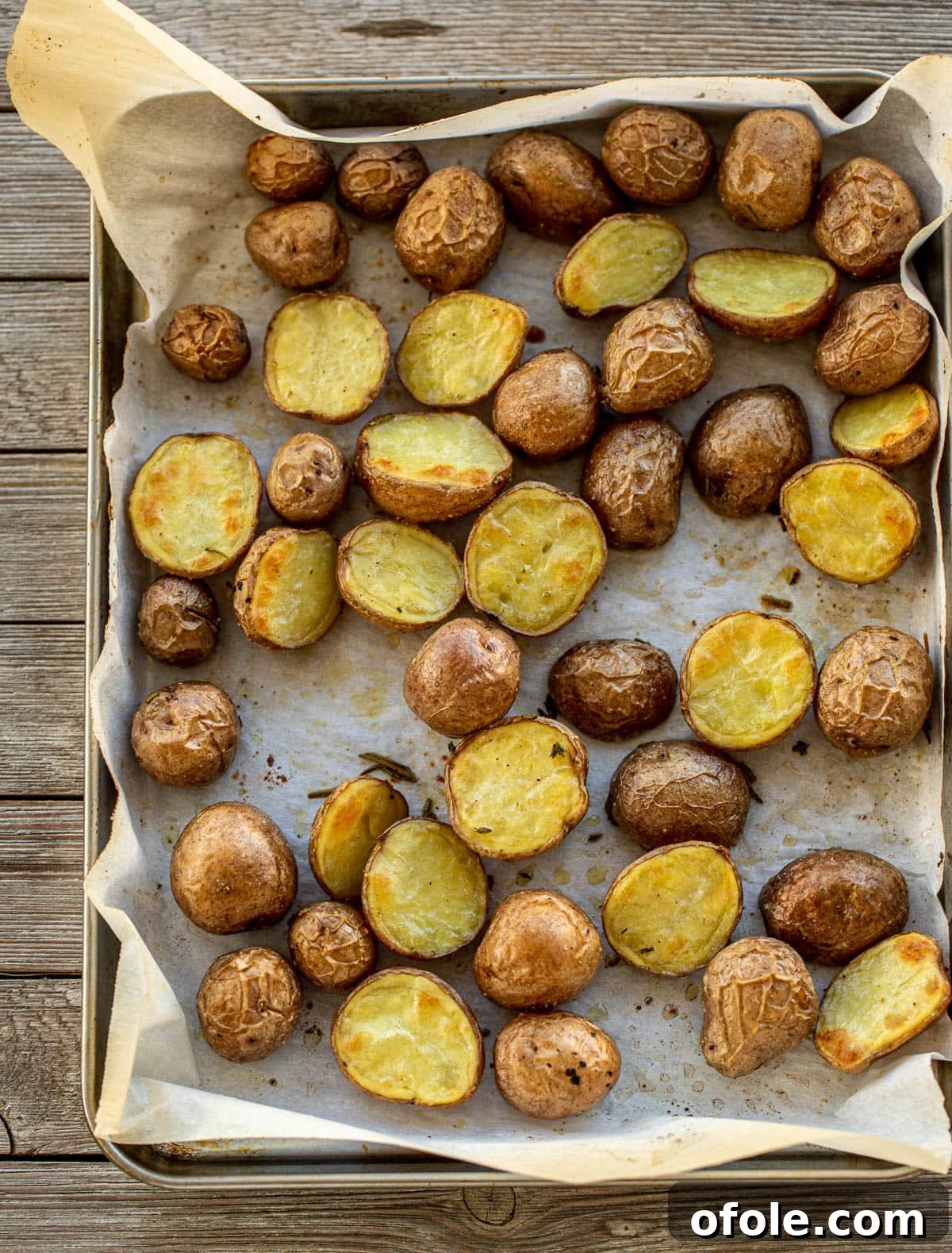 Raw baby potatoes thoroughly tossed with olive oil, garlic, and fresh herbs on a baking sheet lined with parchment paper, ready for the oven