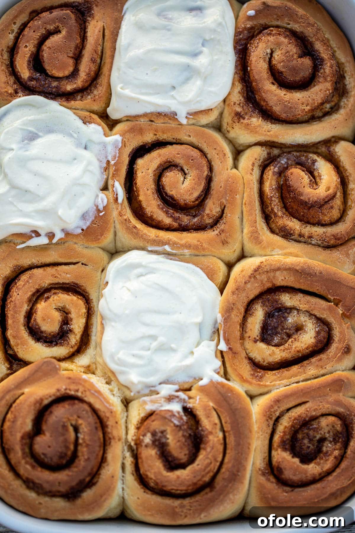 Heavenly Cinnamon Swirls with Tangy Cream Cheese Glaze 2 Cinnamon rolls with cream cheese frosting in a white baking dish.