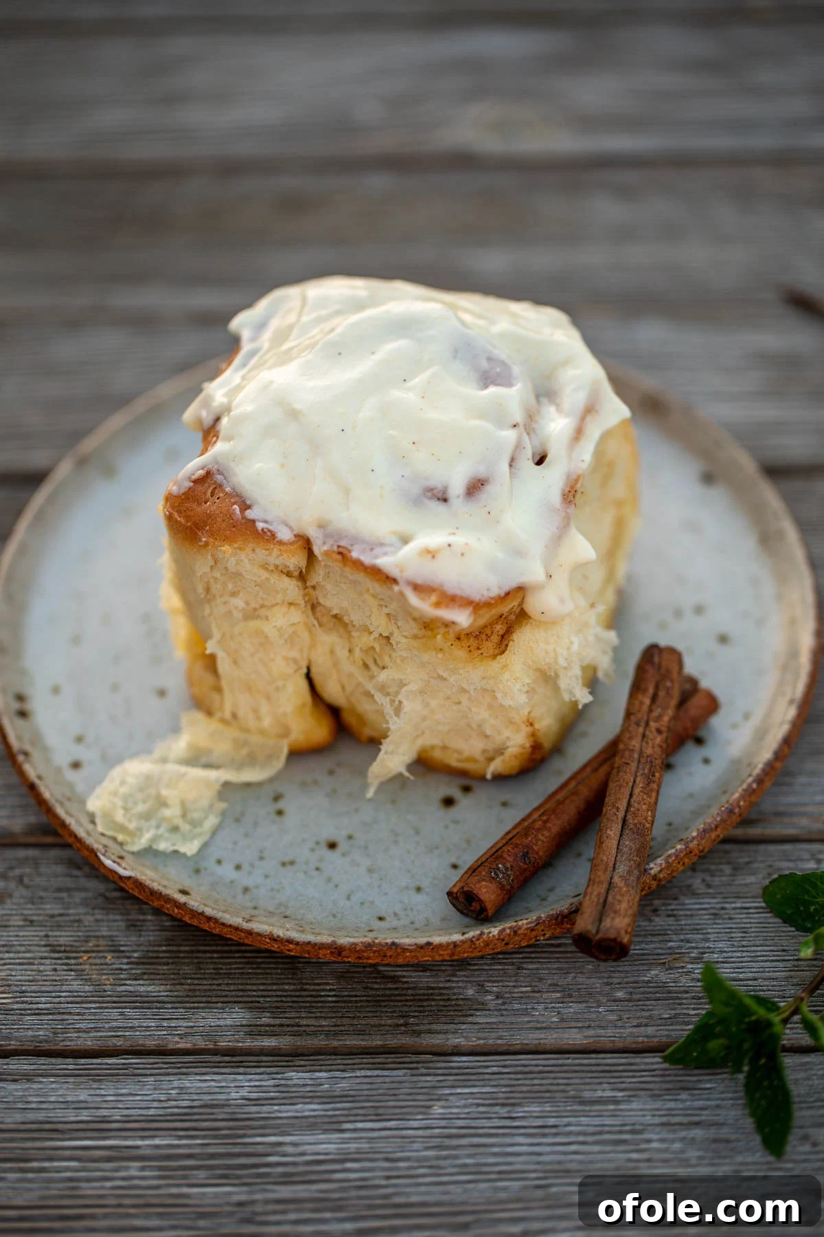 Heavenly Cinnamon Swirls with Tangy Cream Cheese Glaze 3 A cinnamon roll on a plate, topped with cream cheese frosting.