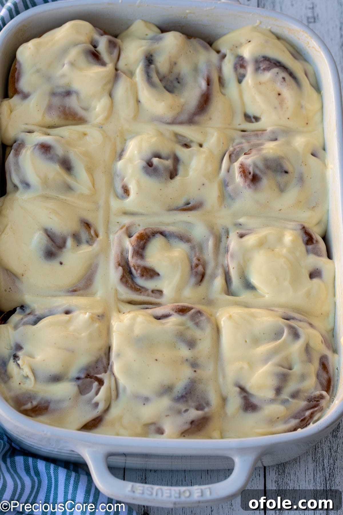 Heavenly Cinnamon Swirls with Tangy Cream Cheese Glaze 5 Cinnamon Rolls completely covered with cream cheese frosting in a white baking dish.