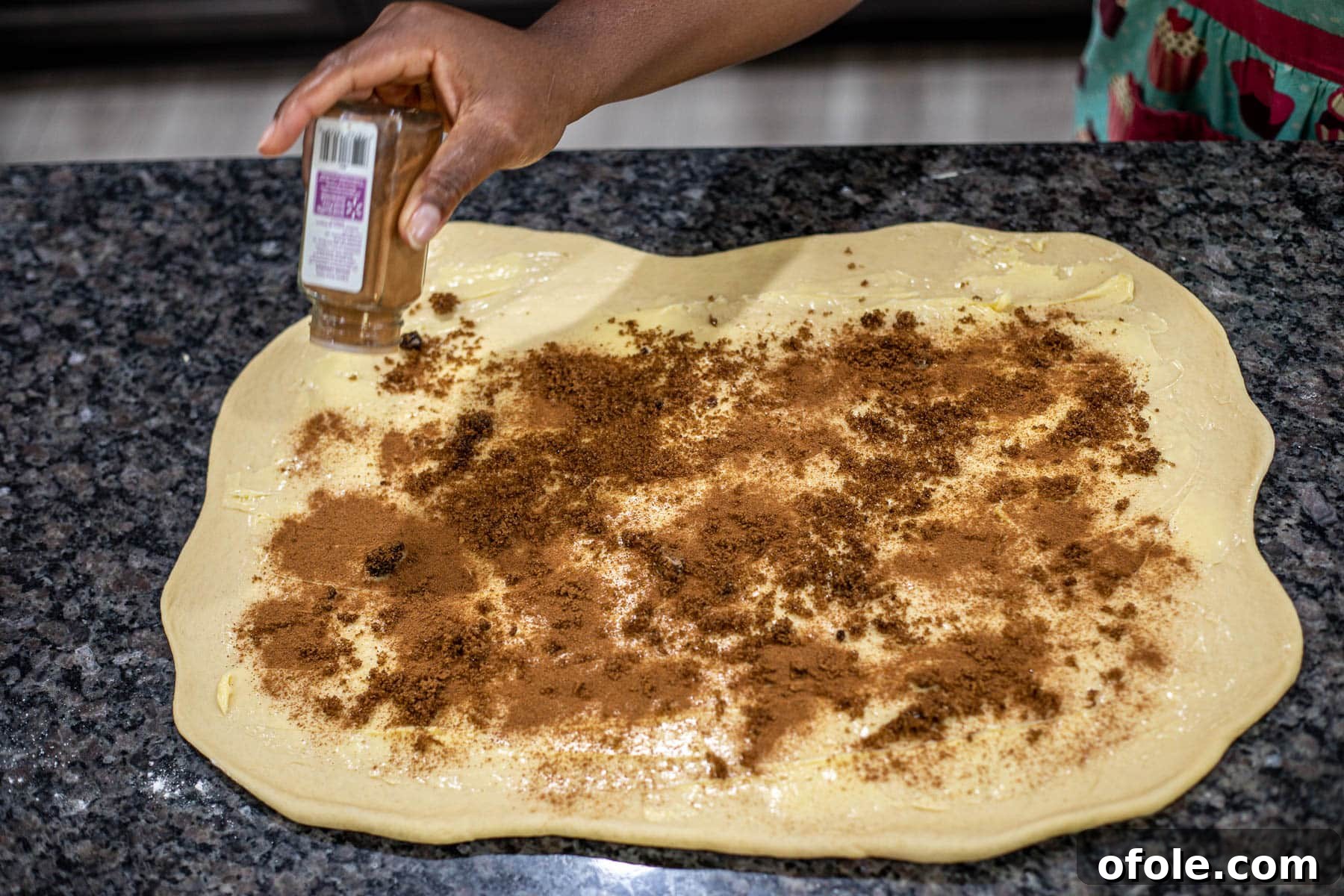 Heavenly Cinnamon Swirls with Tangy Cream Cheese Glaze 9 Hand sprinkling ground cinnamon over dough.