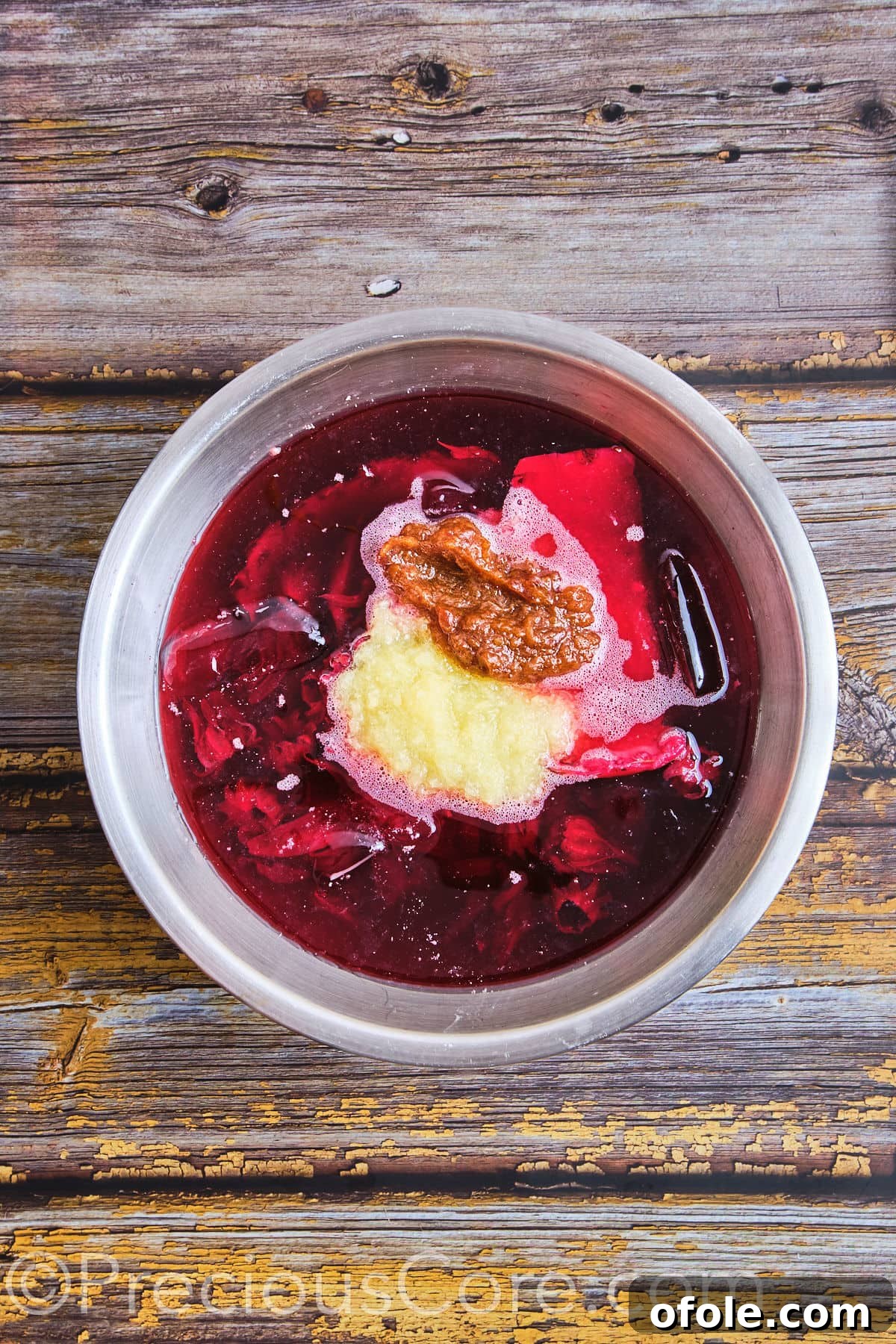 Pineapple and date purees being stirred into a large pot of ruby-red hibiscus tea.