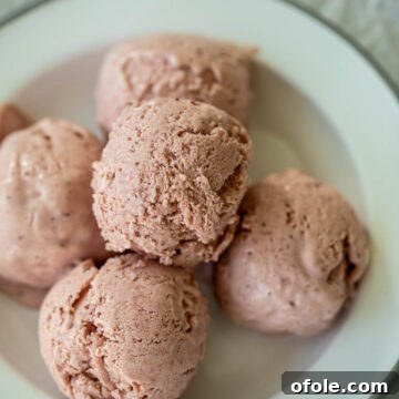 Scoops of vibrant No-Churn Strawberry Ice Cream on a plate, garnished with fresh strawberries