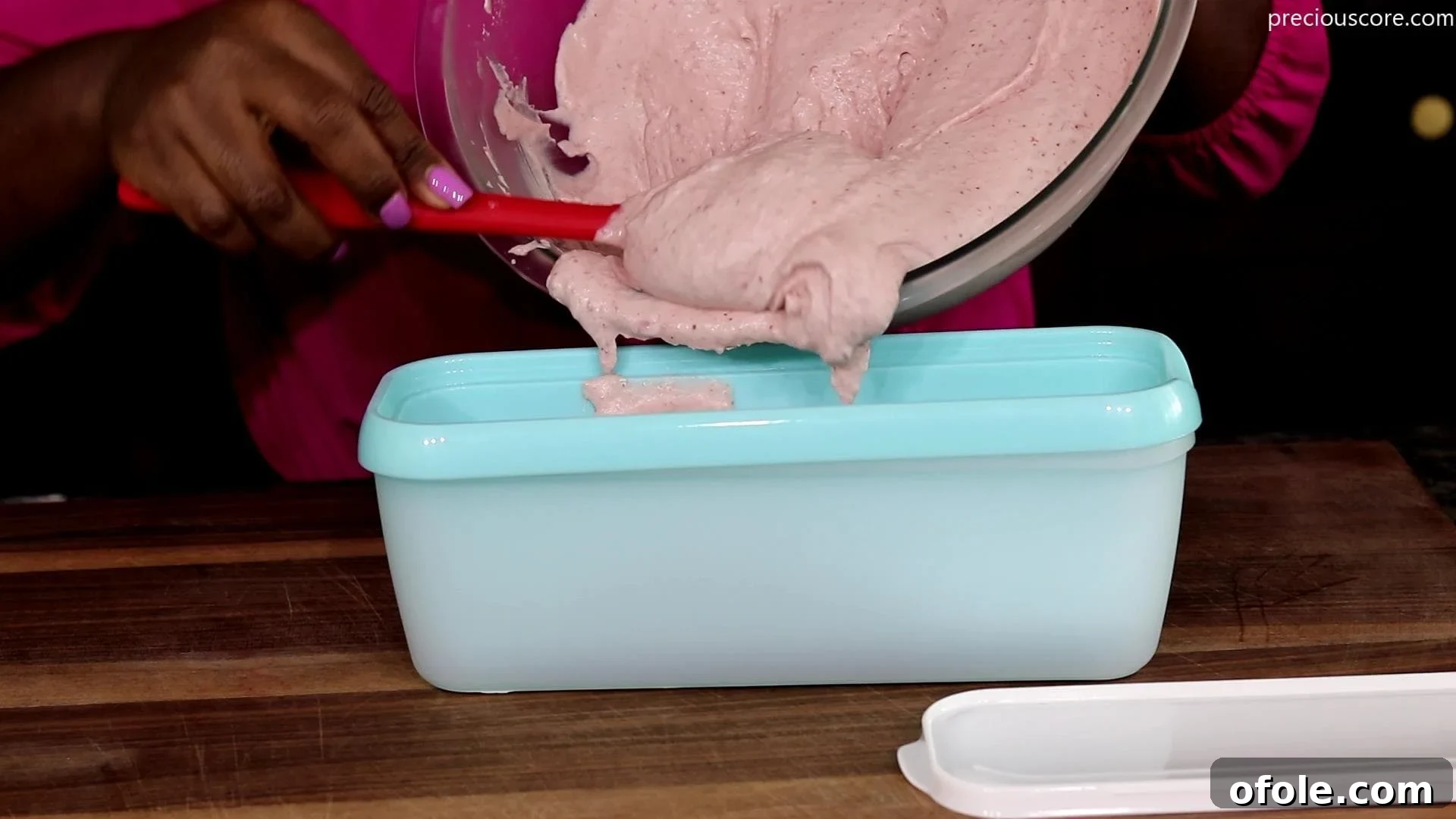 The strawberry ice cream mixture being poured into a loaf pan for freezing.