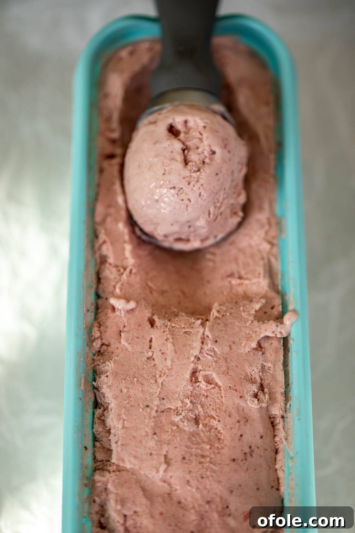 Easy No Churn Strawberry Ice Cream 9 A single scoop of strawberry ice cream resting in a larger bowl of the frozen dessert