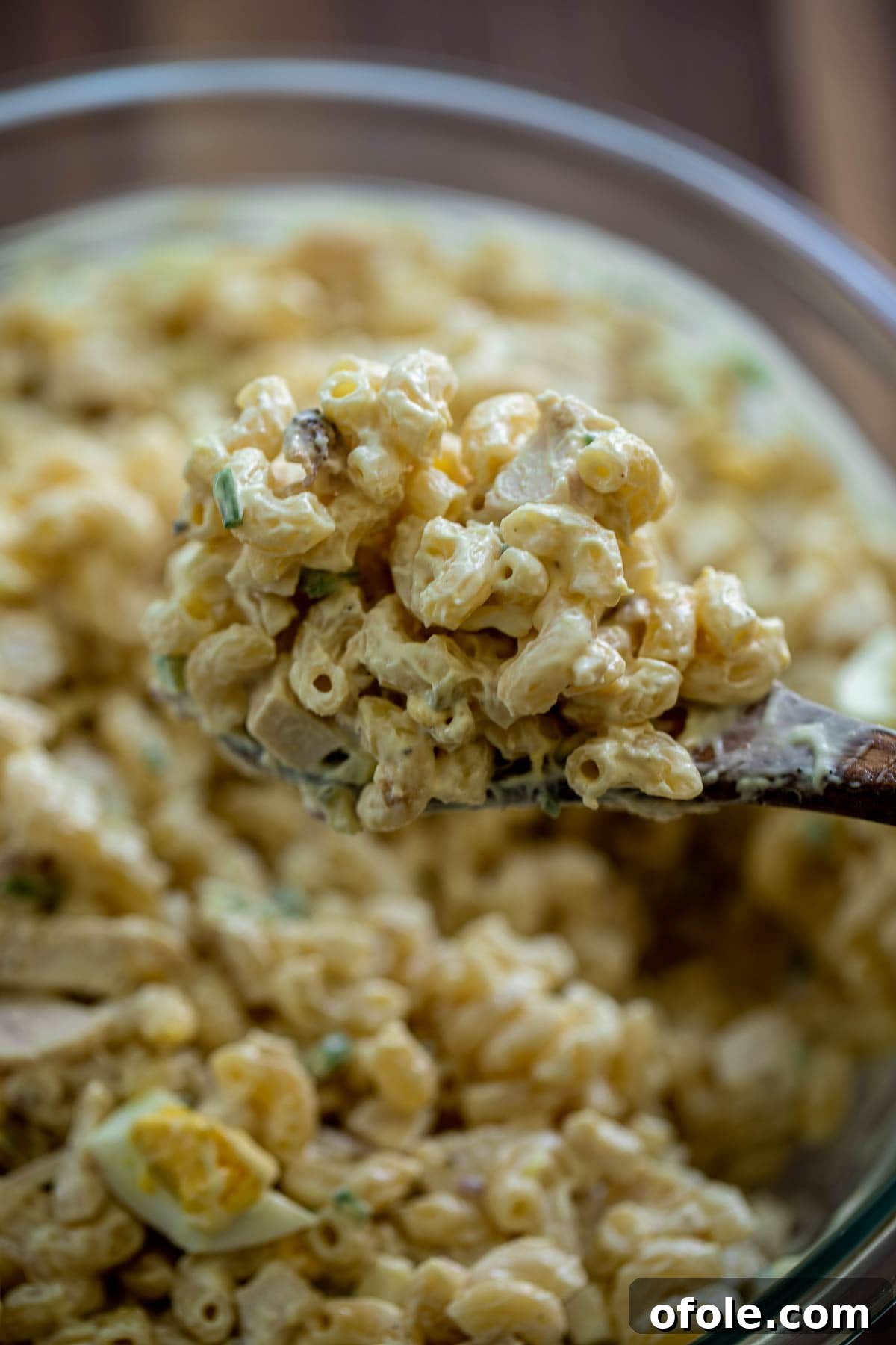 Creamy Chicken Pasta Delight 3 Wooden spoon lifting a portion of creamy macaroni salad with chicken and vegetables.