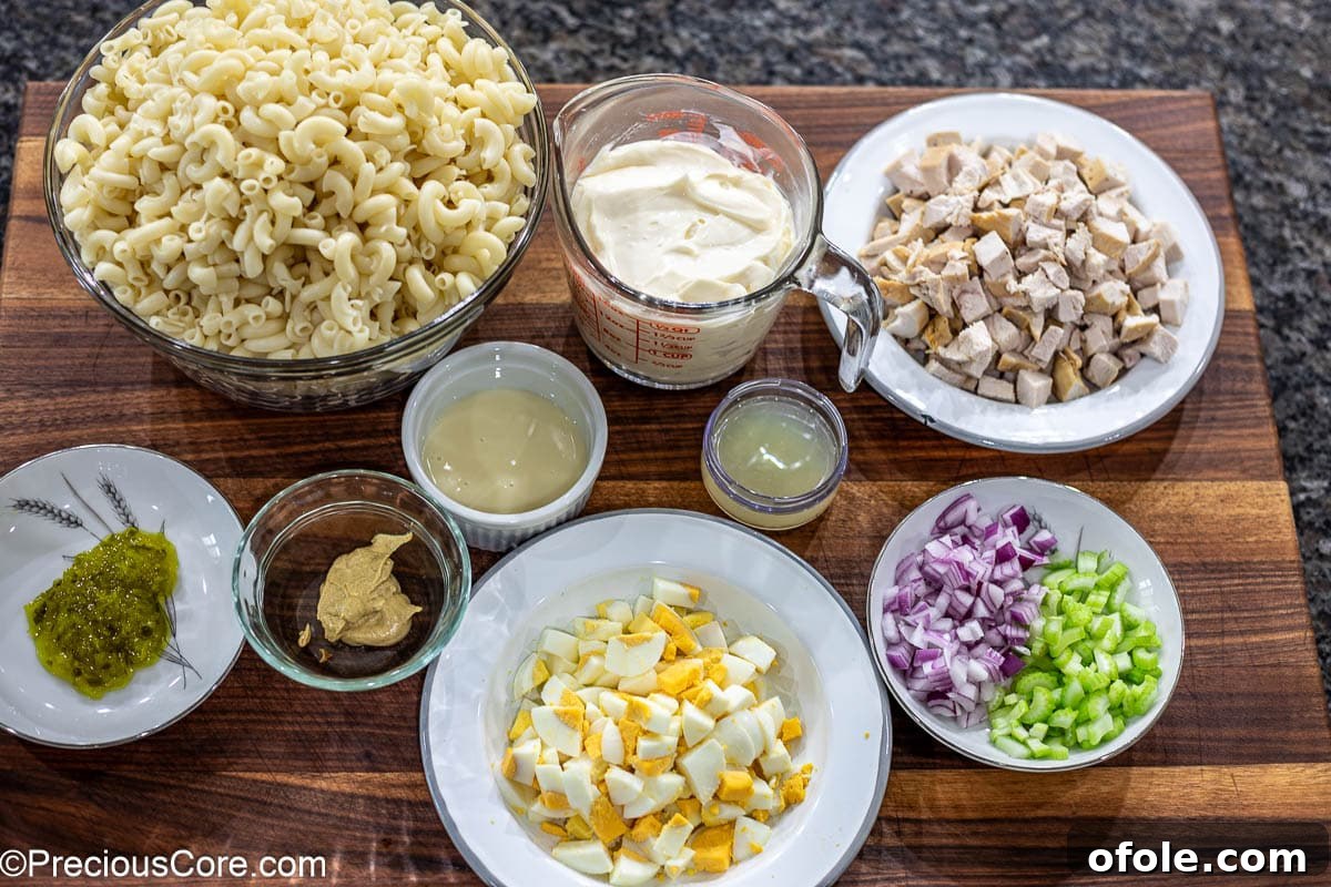 Creamy Chicken Pasta Delight 4 Ingredients for macaroni salad laid out on a chopping board including pasta, chicken, eggs, mayonnaise, lemon, and vegetables.