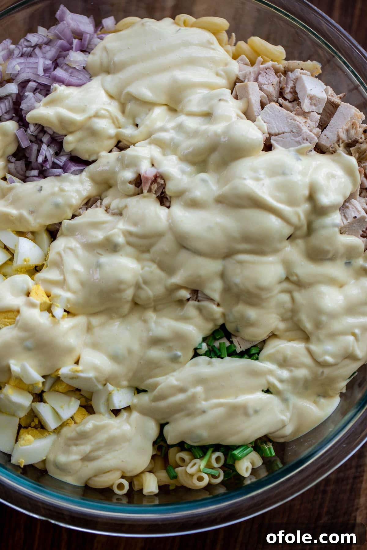 Creamy Chicken Pasta Delight 7 Creamy dressing being poured over the salad ingredients in a bowl.