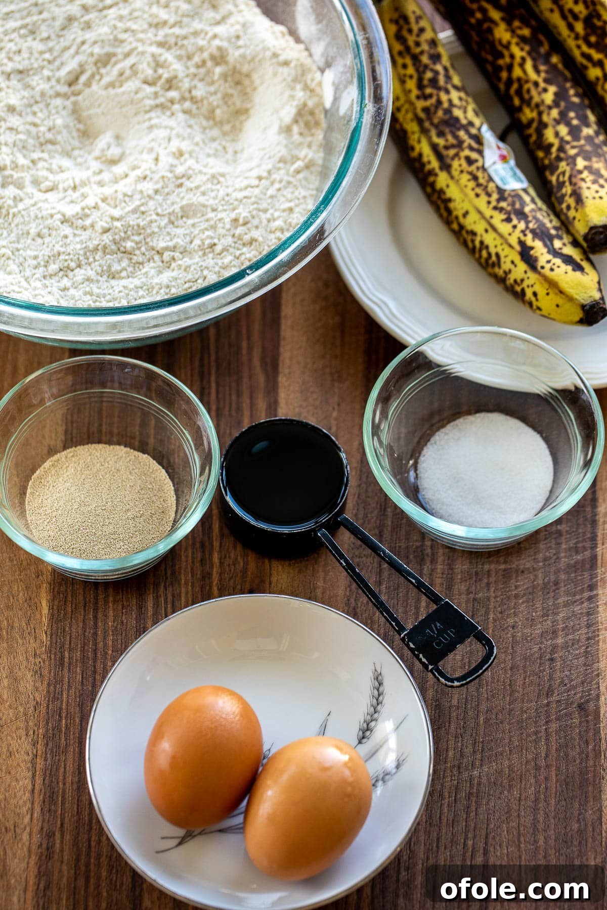 Golden Banana Bread Rolls 3 Key ingredients for banana bread rolls laid out on a wooden chopping board, including bananas, eggs, oil, flour, yeast, and salt.