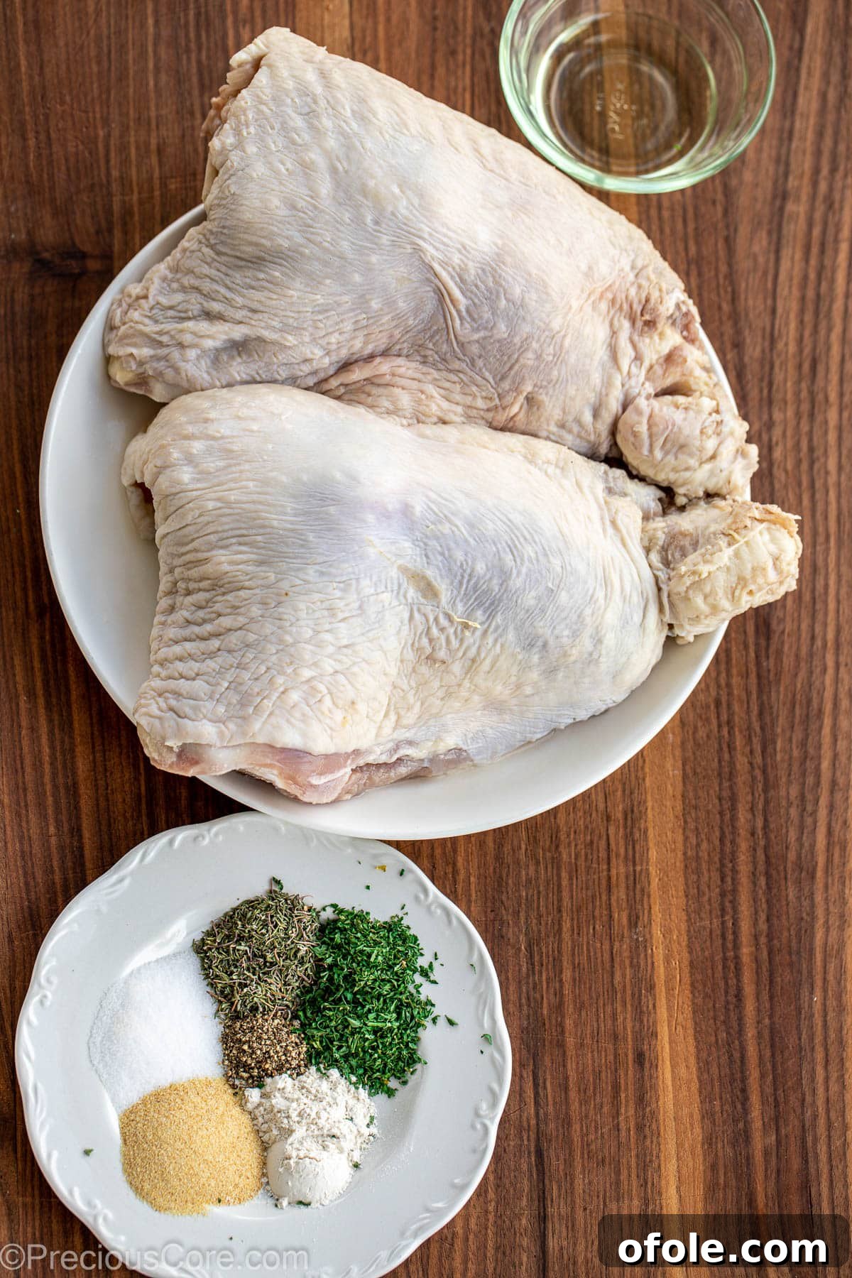 Turkey thighs, a variety of spices, fresh herbs, and olive oil artfully arranged on a chopping board.