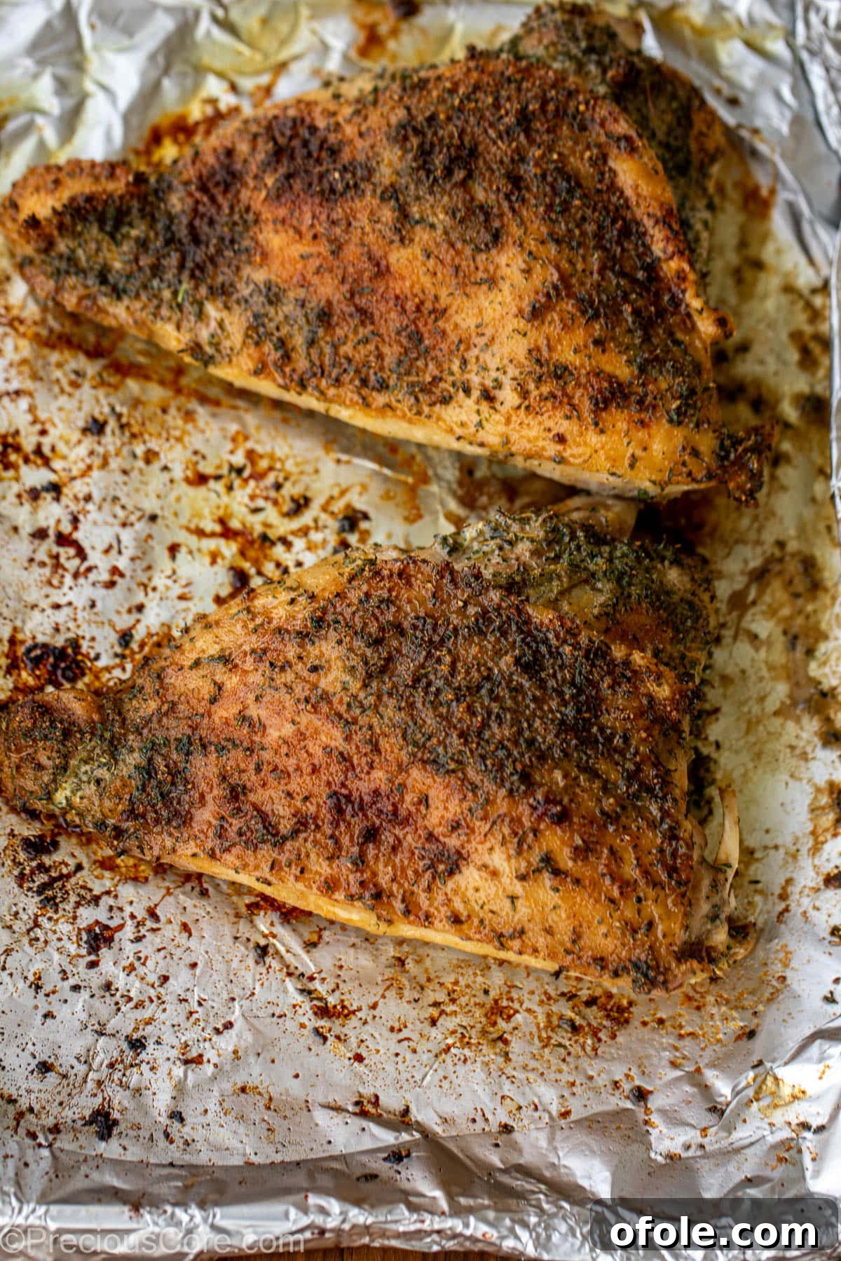 Golden-brown roasted turkey thighs cooling on a tray lined with aluminum foil, juices glistening.