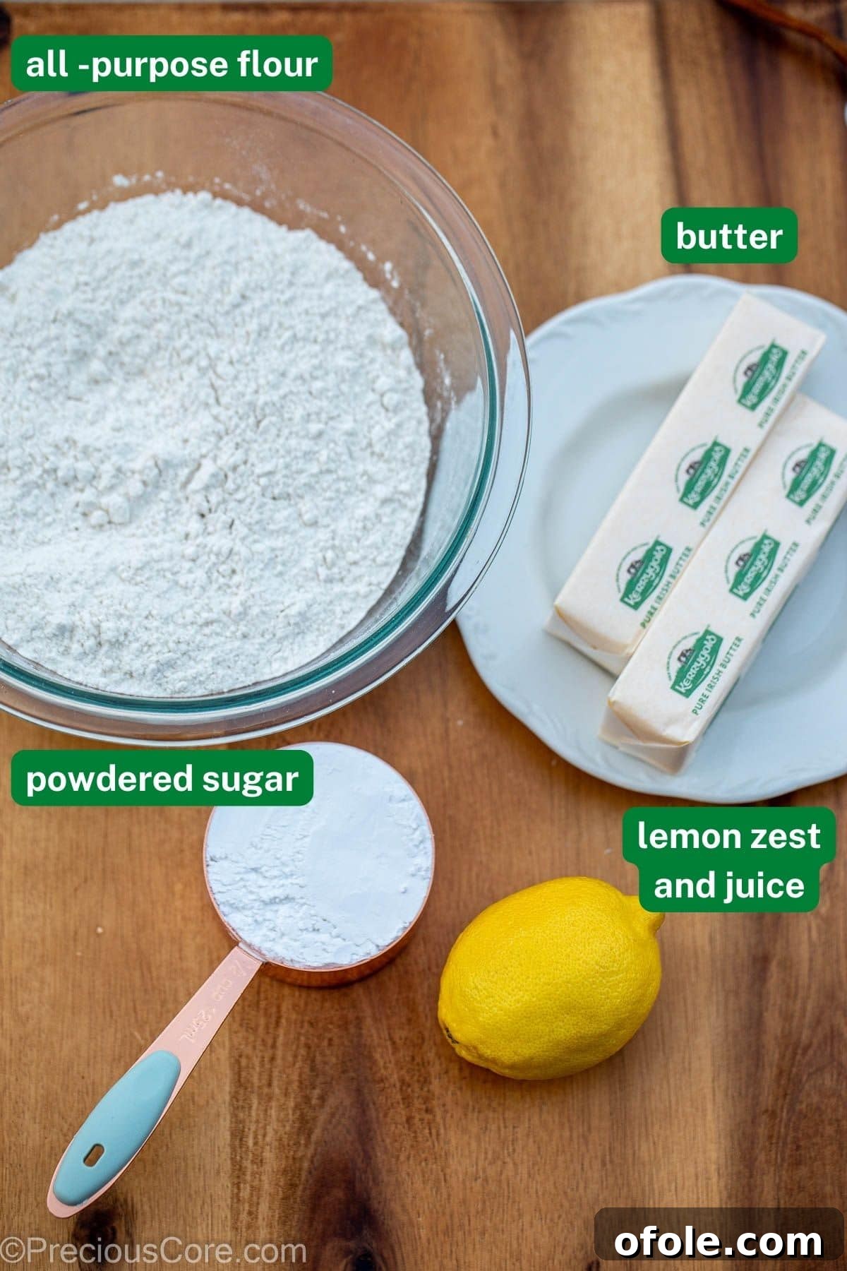Fresh lemons, unsalted butter, all-purpose flour, and powdered sugar arranged on a rustic wooden board.