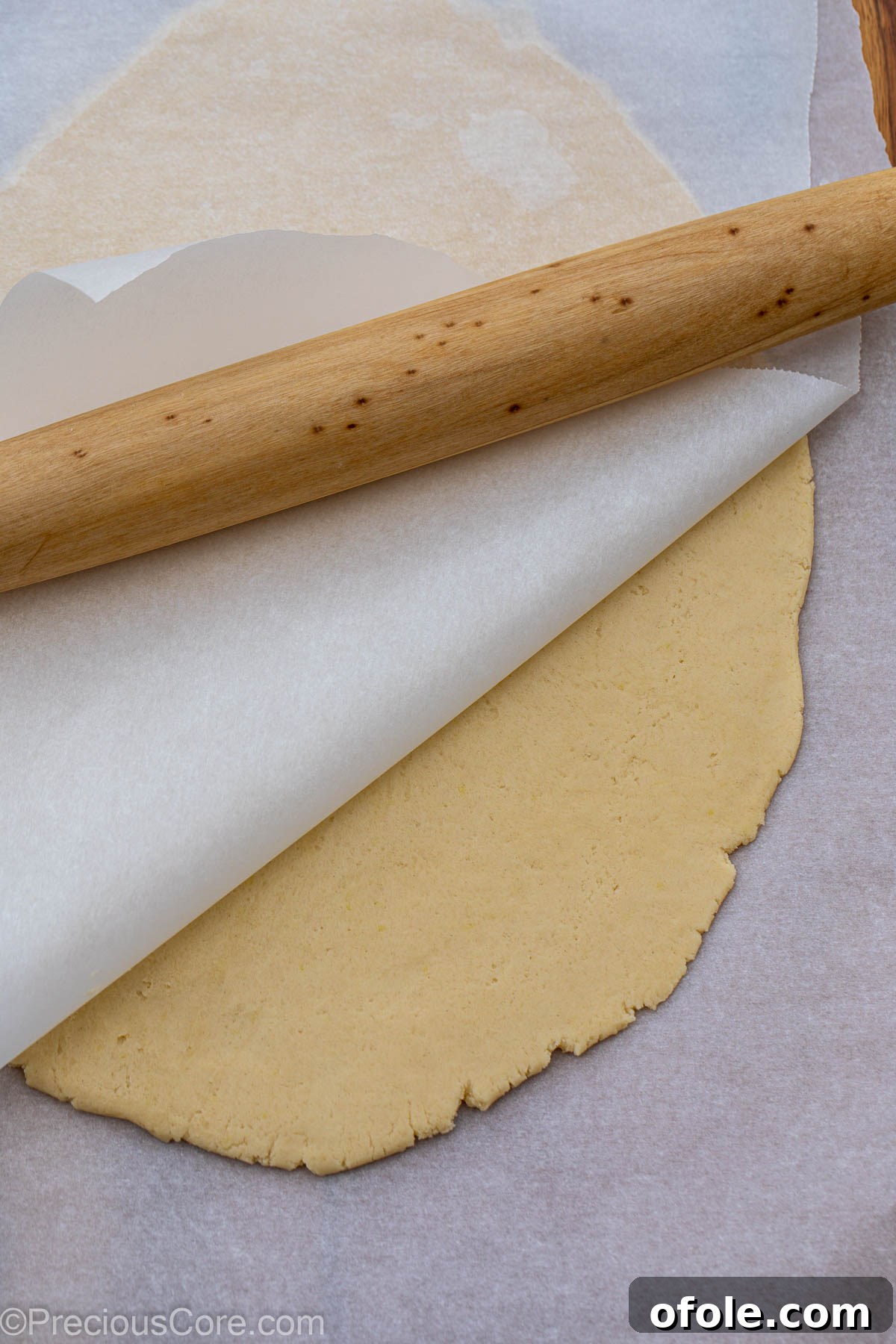 Shortbread cookie dough rolled evenly to a quarter-inch thickness between two sheets of parchment paper.